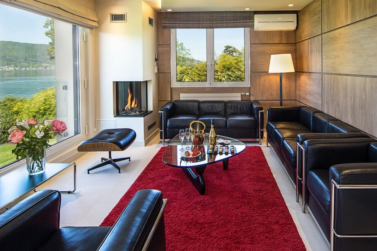 A modern living room with a fireplace, leather sofas, a glass coffee table with snacks, and a view of a lake.