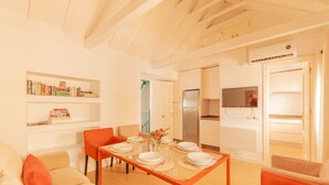 Un soggiorno moderno e luminoso con un tavolo da pranzo per quattro persone, un divano e un angolo cottura con frigorifero e pensili.