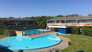 Ein Schwimmbad mit Holzterrasse, umgeben von einem gepflegten Rasen und einem Gebäude mit Balkon.