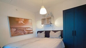 Ein Schlafzimmer mit einem großen Bett, einem Nachttisch, einem Kleiderschrank, einer Deckenleuchte und einem an der Wand befestigten Regal.