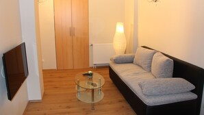 Un soggiorno con un divano, un tavolino in vetro, una TV a parete e una porta in legno.
