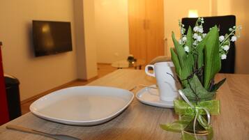 Ein Esstisch mit einem weißen Teller, einer weißen Tasse und einer Glasvase mit grünen Blättern und weißen Blüten.