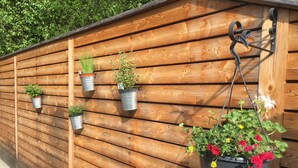 A wooden wall with multiple metal planters of varying sizes, some with plants and flowers.
