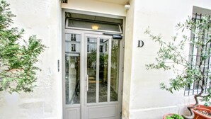 A grey double door with a glass panel, a small window with a metal grid, and a potted plant to the right. - Superb 4-room apartment (Paris)