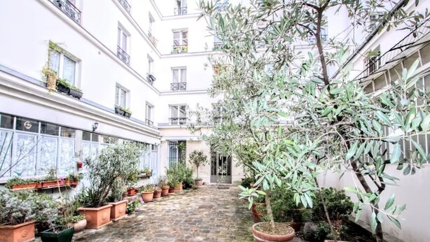 A courtyard with potted plants, a cobblestone path, and a building with balconies. - Superb 4-room apartment (Paris)