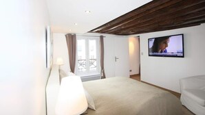 A bedroom with a bed, a TV mounted on the wall, a window with curtains, and a wooden ceiling. - Superb 4-room apartment (Paris)