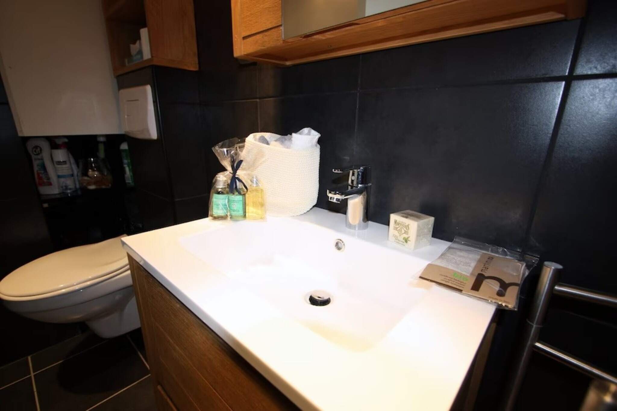 A bathroom with a white sink, a toilet, and a mirror above the sink. There are toiletries on the sink and a towel hanging on the wall.