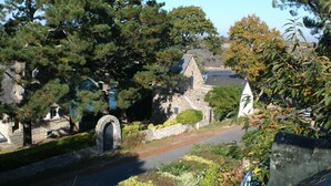 Un bâtiment en pierre doté d’un toit en pente, entouré d’arbres et bordé d’un sentier.