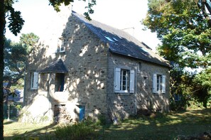 A stone house with a sloped roof, a small porch, and a window with shutters.