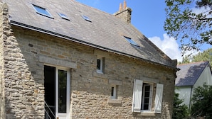 Une maison en pierre avec une terrasse en bois, un escalier et une table entourée de chaises.