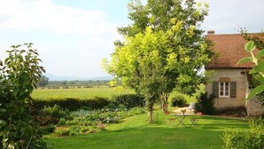 Une maison en pierre avec un jardin, une pelouse et un arbre au premier plan.