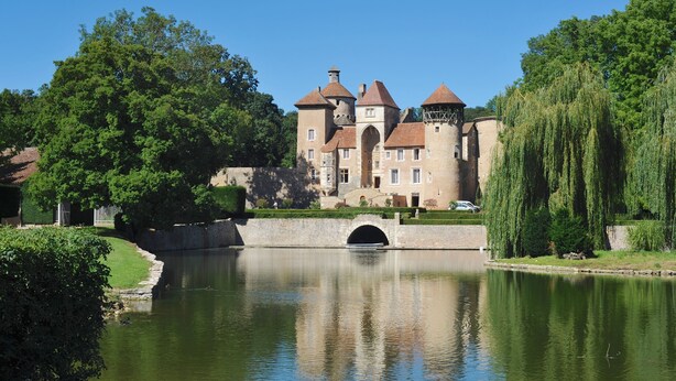 Un bâtiment historique doté d’un fossé, d’un pont en arc et d’une végétation luxuriante.