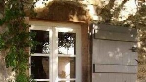 Un bâtiment en pierre doté d’une fenêtre et d’une porte, entouré de verdure et de fleurs.