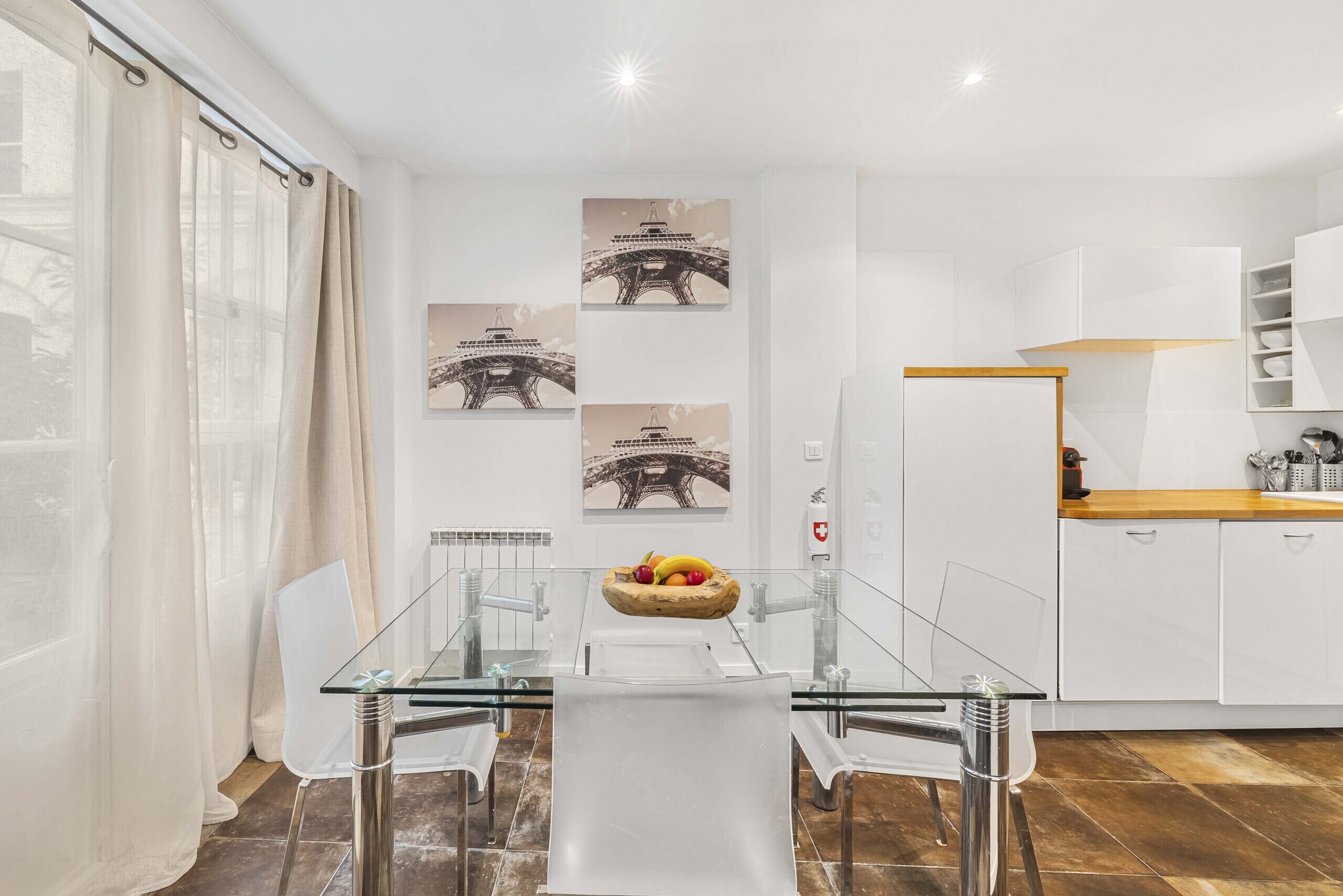 A modern kitchen with white cabinets, a wooden countertop, and a glass dining table with chairs.