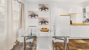 Une cuisine moderne avec des meubles blancs, un plan de travail en bois et une table à manger en verre, accompagnée de chaises.