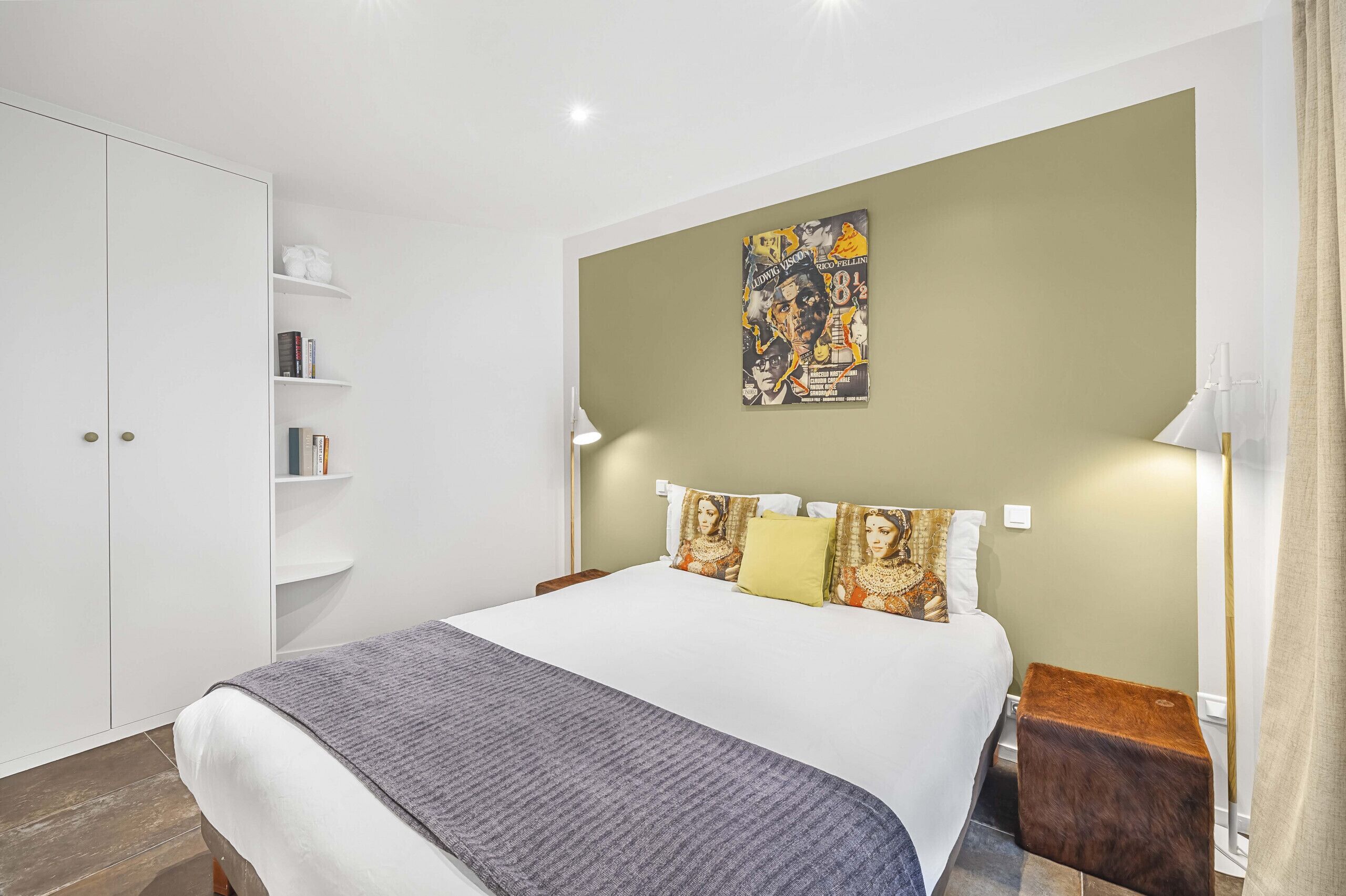 Un dormitorio con cama, armario, mesita de noche, lámpara y un cartel en la pared.