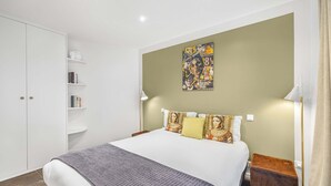 Une chambre à coucher avec un lit, une armoire, une table de chevet, une lampe et une affiche accrochée au mur.