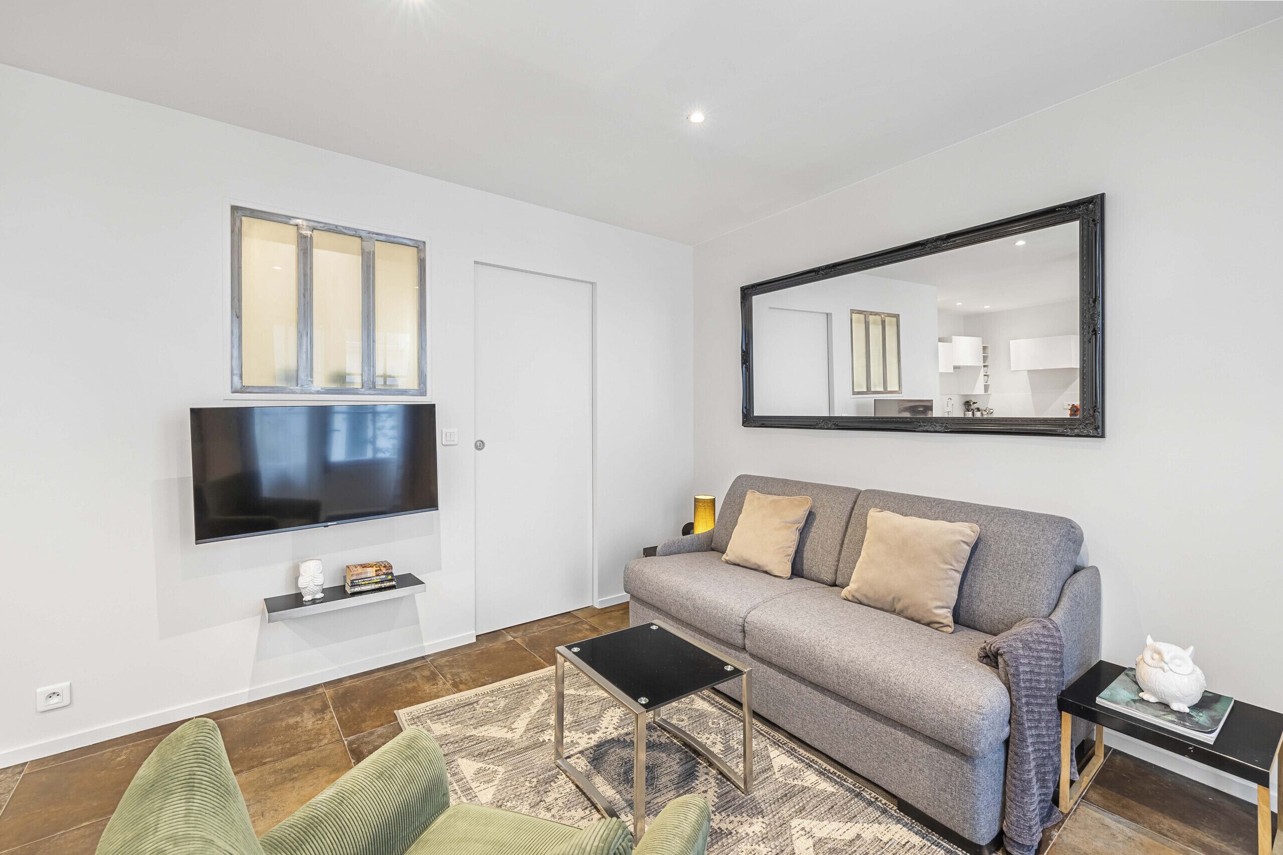 A modern living room with a flat-screen TV, a sofa, a coffee table, and a large mirror.