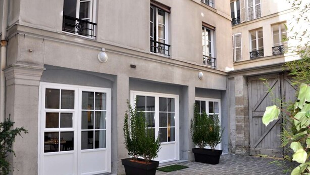 Un bâtiment doté de grandes fenêtres et d’une cour pavée.