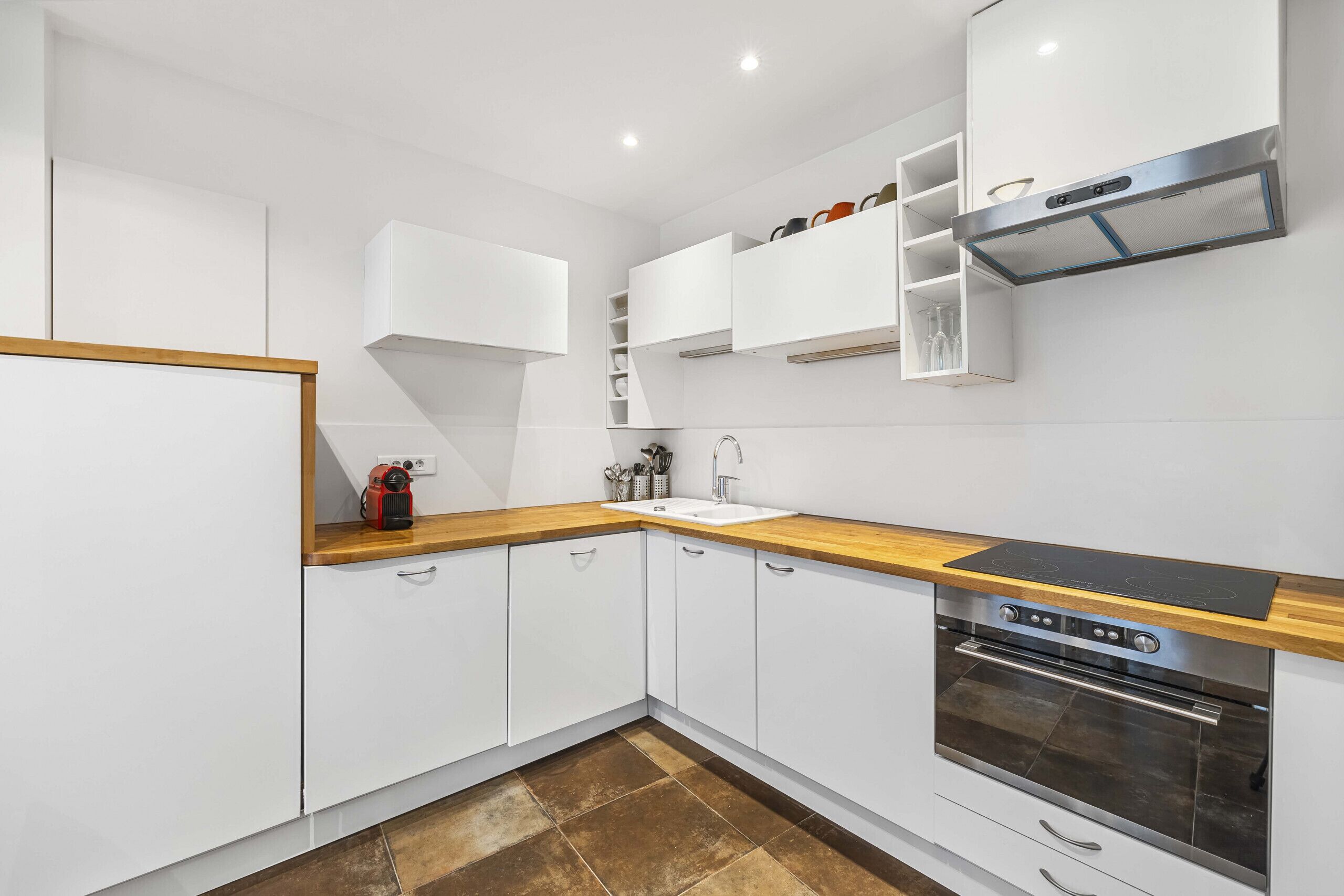 A modern kitchen with white cabinets, a wooden countertop, a built-in oven, and a stainless steel range hood.
