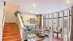 Una sala de estar con una escalera, un conjunto de sofá, una mesa de centro y un ventanal grande.