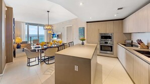 A modern kitchen with a central island, built-in appliances, and a dining area with a view of the sea.