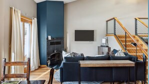 Un salon avec un mur d’accent bleu foncé, une cheminée, un ensemble de canapés, une table en bois et un escalier avec des rampes en bois.