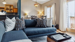 Un salon moderne avec un canapé bleu, une table à manger avec des chaises, un lustre et une vue sur l’extérieur.