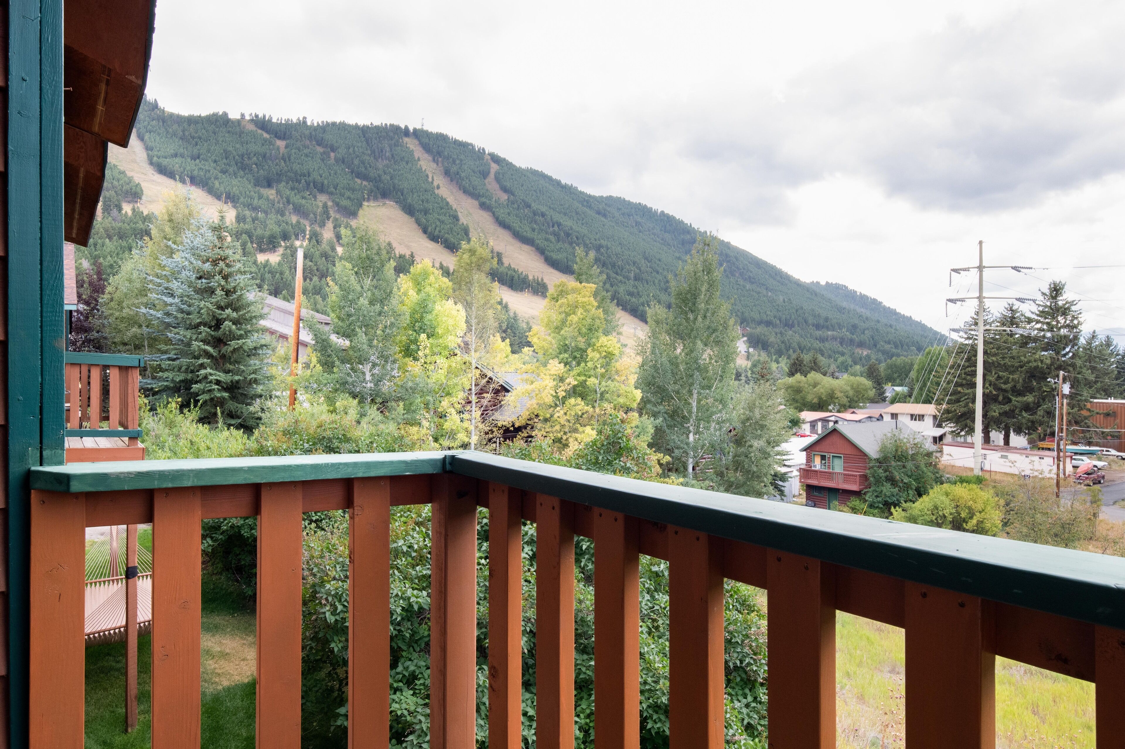A wooden balcony with a view of a mountainous landscape, houses, and trees.
