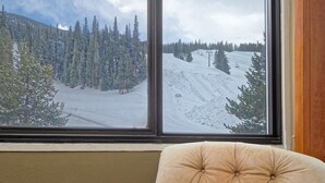 Een raam met uitzicht op een besneeuwd berglandschap, inclusief bomen en een skilift.