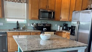 Una cocina con armarios de madera, un refrigerador de acero inoxidable, un microondas y una encimera de granito.