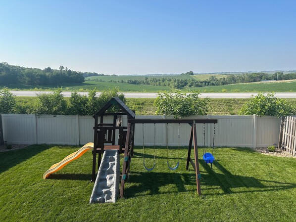 A backyard with a wooden playhouse, a slide, and swings. - 3000 sq ft West Omaha home.  Perfect for wedding parties or families with kids! (Bennington)
