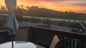 Una terraza con una mesa redonda de vidrio y sillas, con vistas a un paisaje con atardecer.