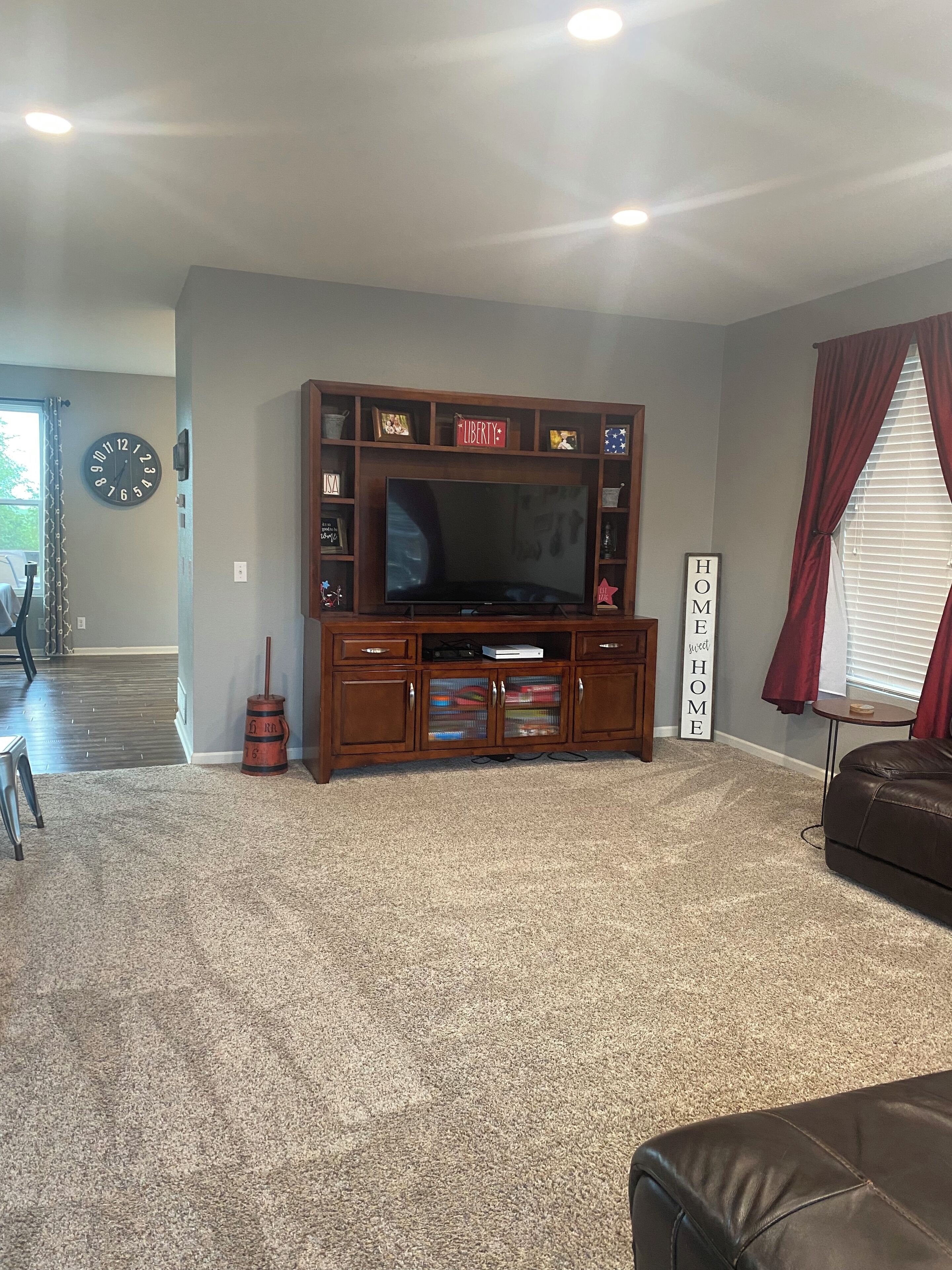 A living room with a large flat-screen TV, wooden entertainment center, and a red curtain.