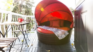 Un área de estar al aire libre con muebles de mimbre, una silla con cojín rojo y una mesa con una taza roja.