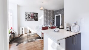 Una cocina moderna con armarios blancos, un comedor con sillas rojas y una obra de arte con un paisaje urbano en blanco y negro en la pared.
