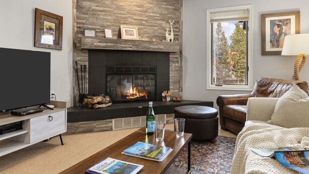 A modern living room with a fireplace, a television, a leather sofa, and a coffee table with magazines. - Outpost: Balsam Lodge A6 (Wilson)
