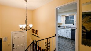 A staircase with a black railing leading to a kitchen area with white cabinets and a wooden floor. - Spacious and comfortable 3 bedrooms house in the heart of Overland Park (Overland Park)
