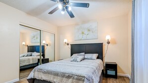 A bedroom with a bed, a ceiling fan, a large mirror, and two bedside lamps. - Spacious and comfortable 3 bedrooms house in the heart of Overland Park (Overland Park)