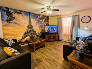 A living room with a large mural of the Eiffel Tower, a television, a ceiling fan, and a clock on the wall. - Spacious and comfortable 3 bedrooms house in the heart of Overland Park (Overland Park)