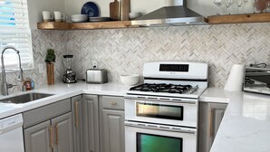 A modern kitchen with white cabinetry, a stainless steel range hood, and a herringbone-patterned backsplash. -  COZY BEACH HOUSE plus  GUEST HOUSE 
each unit 2 adults  PET FRIENDLY (Santa Cruz)