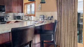 A kitchen with wooden cabinets, a granite countertop, a coffee maker, and a window with curtains. - Outpost: Sleeping Indian E10 - Hot Tub Access! (Teton Village)