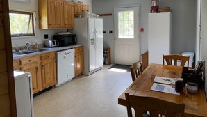 Une cuisine compacte avec des meubles en bois, un réfrigérateur blanc, un four à micro-ondes et un lave-vaisselle. On y trouve une table à manger avec des chaises et une fenêtre qui laisse entrer la lumière naturelle.