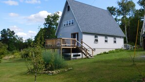 Une maison avec un toit à forte pente, une terrasse en bois et un petit escalier menant à l’entrée.