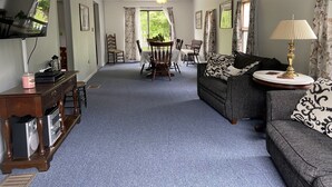 Un salon comprenant un canapé, une table basse, un téléviseur fixé au mur et un coin repas avec des chaises et une table.