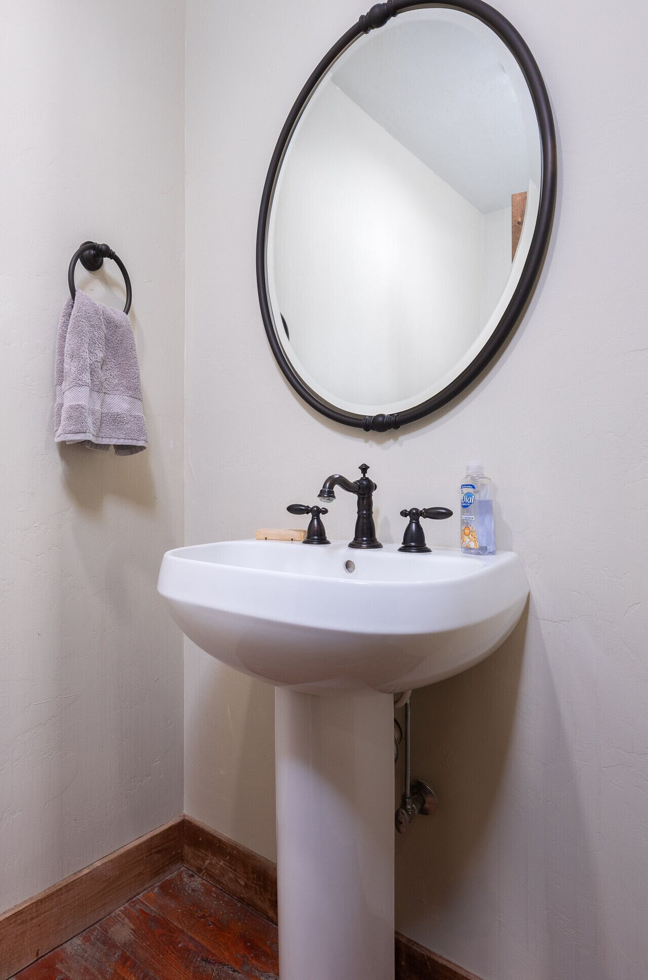 Un baño con un lavabo blanco, dos grifos negros, un espejo redondo y una toalla colgada en un aro de metal.