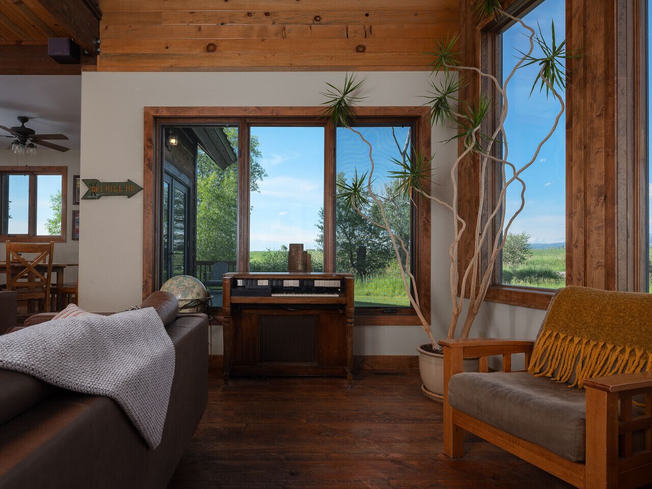 Een gezellige woonkamer met een piano, een bank, een fauteuil en een groot raam met uitzicht op de natuur.