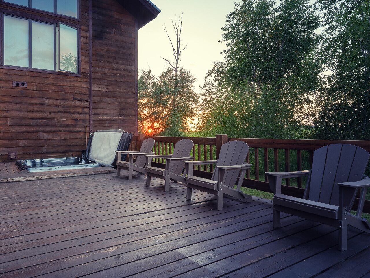 A wooden deck with Adirondack chairs and a hot tub.