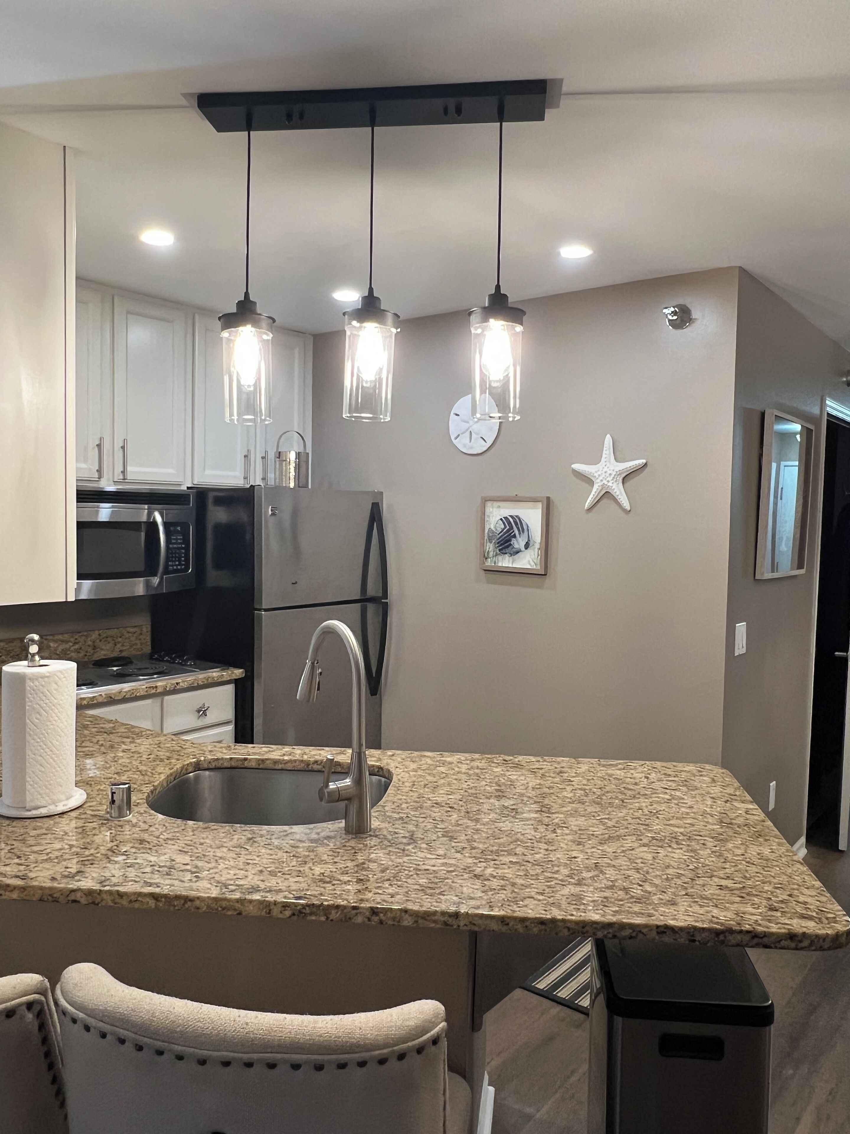 A modern kitchen with granite countertops, stainless steel appliances, pendant lighting, and decorative wall art.