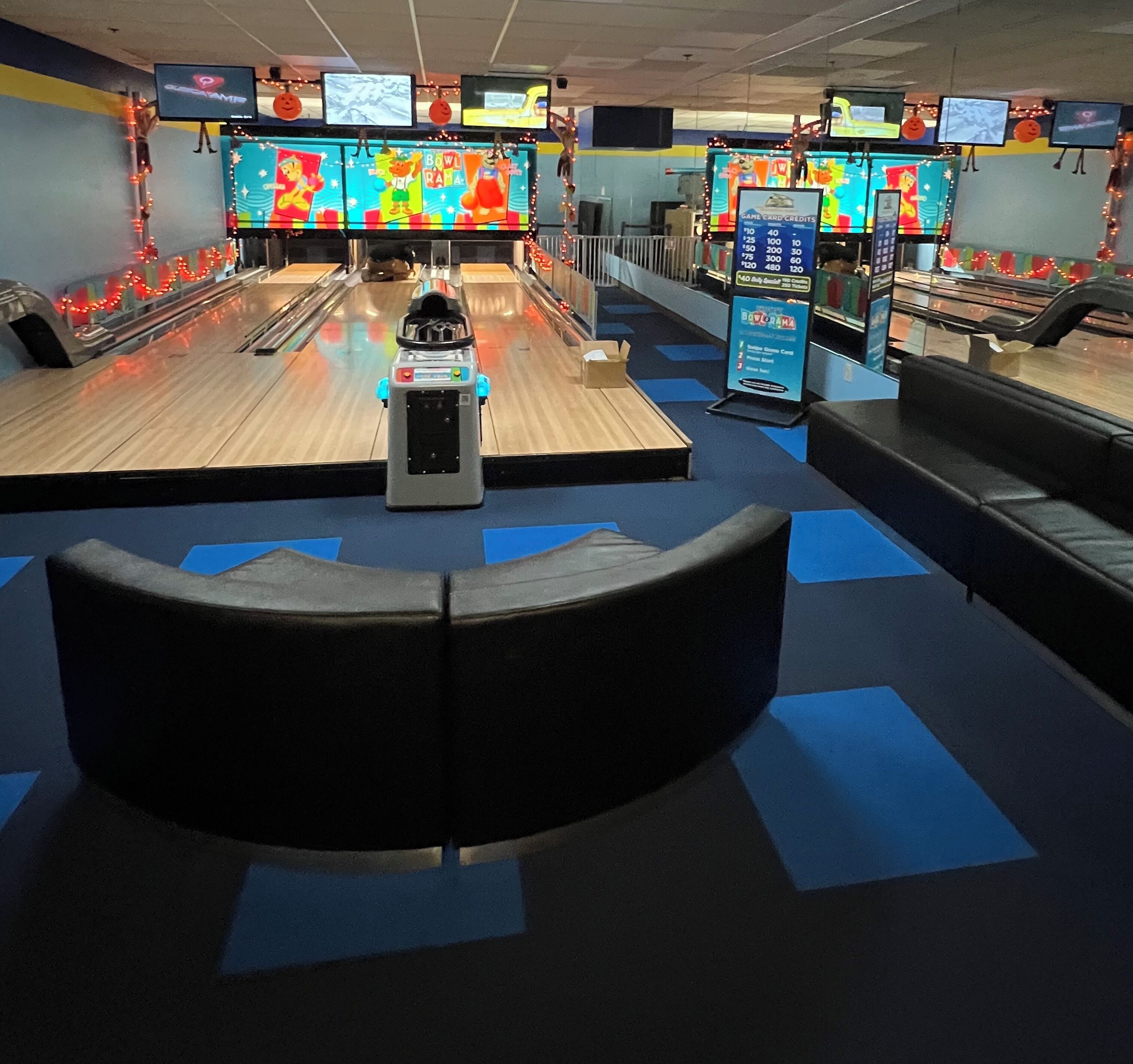 A bowling alley with multiple lanes, a bowling ball return system, and several monitors displaying games.